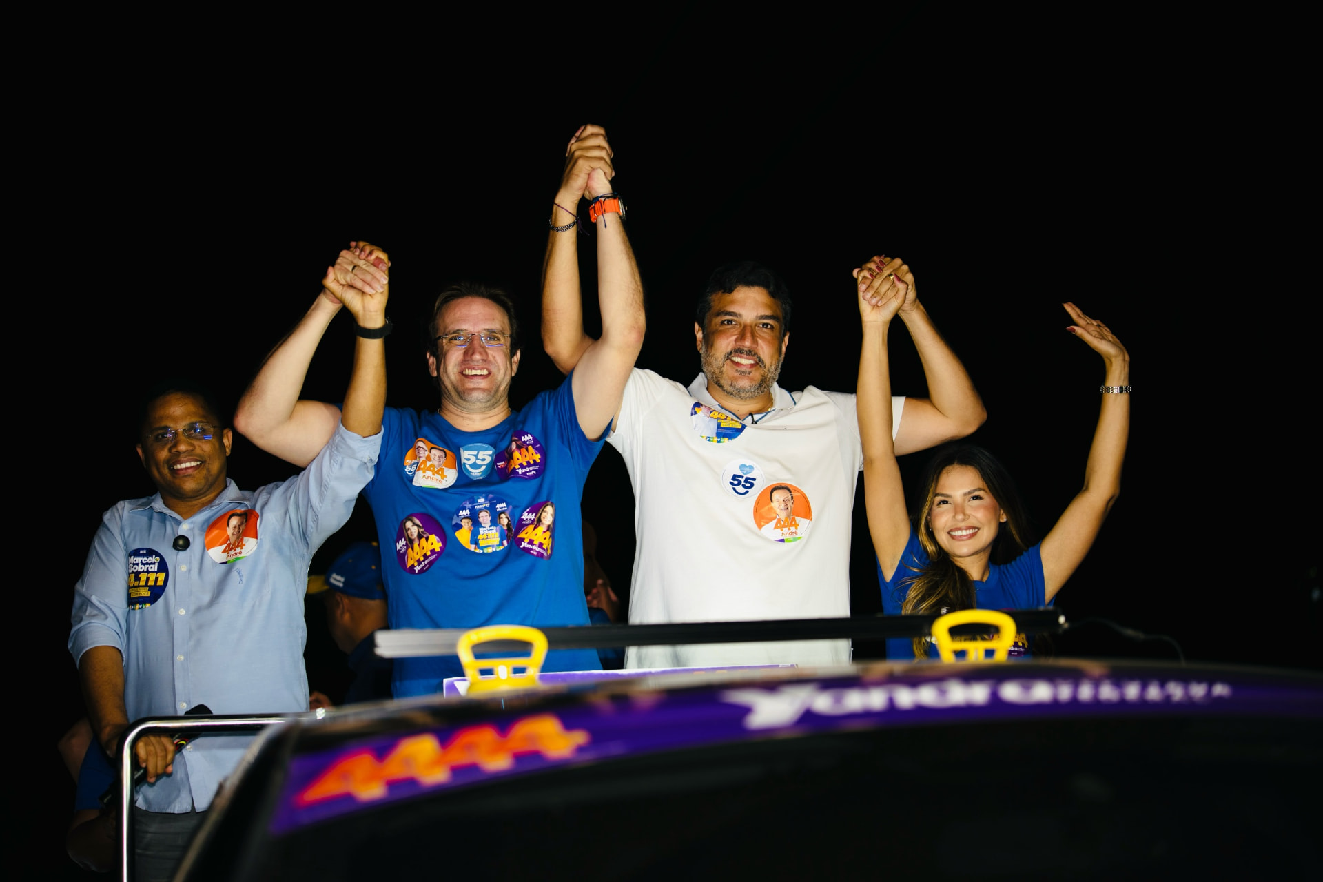 Marcelo Sobral e participantes de mãos erguidas no veículo da carreata à noite